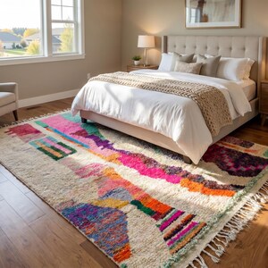 May include: A rectangular area rug featuring a cream-colored base with an abstract pattern of vibrant geometric shapes in shades of hot pink, orange, teal, purple, and blue. The rug has a thick, textured pile and includes fringe along the edges.