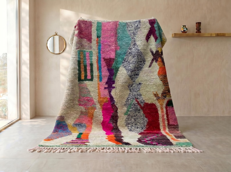 May include: A large rectangular area rug featuring a cream-colored base with an abstract pattern of vertical stripes and geometric shapes in vibrant shades of hot pink, teal, orange, purple, and dark gray, finished with a knotted fringe at the bottom.