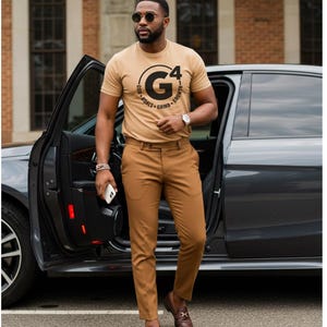 May include: A tan crew neck t-shirt with the text "G4" in a black circle, paired with brown pants and brown leather loafers. The person is wearing sunglasses and a watch. A black car is in the background.