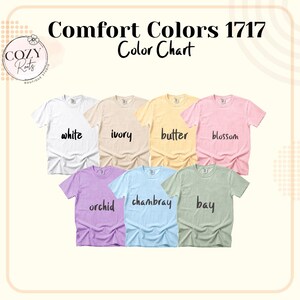 May include: A Comfort Colors 1717 colour chart featuring seven short-sleeve t-shirts in white, ivory, butter, blossom, orchid, chambray, and bay. The text Comfort Colors 1717 Colour Chart is displayed at the top with a Cozy Roots logo in the corner.