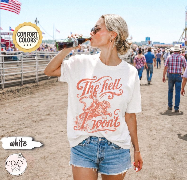 May include: A white short-sleeve t-shirt featuring a red graphic print of a tiger and the text The hell I won't. The shirt is paired with blue denim shorts. The graphic design includes stylized lettering and a tiger illustration on the front.