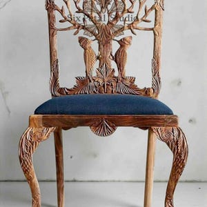 May include: A wooden chair with intricate carvings. The back features a tree design with birds, and the seat is upholstered in blue fabric. The legs are curved and detailed with floral patterns. The chair has the text "Six Petal Studio".