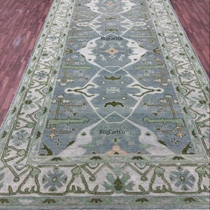 Peut inclure: Un tapis rectangulaire avec un champ central bleu clair orné d'un motif symétrique blanc, vert et beige. La bordure présente des motifs géométriques verts et blancs. Le tapis a une frange aux deux extrémités.