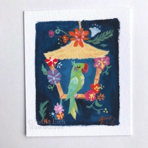 May include: A green parrot with a red beak sits in a bamboo birdhouse decorated with colourful flowers. The birdhouse has a straw roof and is hanging from a string. The background is a dark blue.