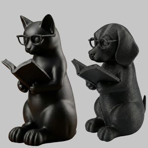 May include: Two black figurines: a cat and a dog, both wearing glasses and reading books. The cat is on the left, and the dog is on the right. The figurines are set against a gray background.