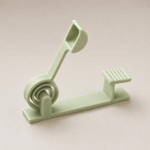 May include: A sage green plastic object featuring a flat base, a circular hinge mechanism, an angled arm with a small scoop-like end, and a separate horizontal platform with a ribbed surface texture, all constructed as a single solid unit.