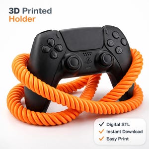 May include: A black game controller is held by a bright orange, coiled holder. The text "3D Printed Holder" is at the top left. The bottom right corner has the text "Digital STL", "Instant Download", and "Easy Print".