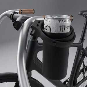 May include: A black bicycle with a custom-designed drink holder attached to the handlebars. The holder securely cradles a silver and white energy drink can. The handlebars are silver with brown leather grips.