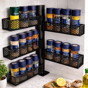 May include: Black metal spice rack with a honeycomb design, holding various spice jars with blue lids. The rack is mounted on a white tiled wall, showcasing a kitchen organization theme.