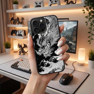 May include: A black phone case with a white dragon illustration. The design shows a detailed dragon with scales and flowing elements. The case has a black border and is held in a hand with white nail polish. The case is designed for a smartphone.