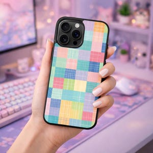 Puede incluir: Una funda de teléfono negra con un diseño de patchwork colorido. La funda presenta un patrón de cuadrados en tonos pastel de rosa, azul, amarillo y verde. La funda del teléfono se sostiene en una mano.