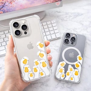Può includere: Custodie trasparenti per telefono con un design stravagante con oche bianche con becchi gialli. Le custodie sono mostrate su una superficie di marmo, con un computer e una tastiera sullo sfondo. Progettate per un iPhone Apple.