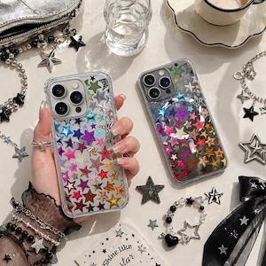 May include: Two clear phone cases with star patterns in various colours. The cases feature stars in red, orange, yellow, green, blue, and purple. Star-shaped jewellery and a small bag are also visible, creating a celestial theme.