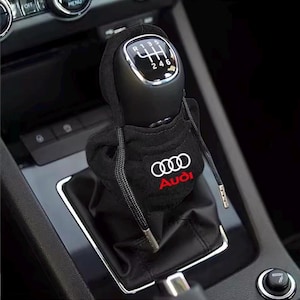 Peut inclure: Housse de levier de vitesse noire avec le logo Audi blanc et rouge. La housse est en matière souple et possède un cordon de serrage. Le pommeau de levier de vitesse est noir avec des indications de vitesse blanches.