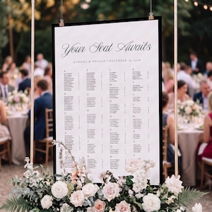 May include: A vertical wedding seating chart sign with a white background and black text. The header reads Your Seat Awaits, followed by Aurora & Phillip | December 10, 2026. Names are listed alphabetically under lettered columns.