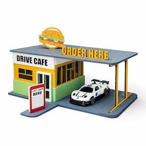 May include: A miniature drive-in cafe model with a burger on top. The cafe has a green and yellow facade, with the words "DRIVE CAFE" and "ORDER HERE" displayed. A white race car is parked under the awning, and a "Fast Food Menu" sign is visible.
