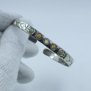 May include: A silver cuff bracelet featuring five opal gemstones. The bracelet has a geometric pattern and is open at the bottom. The opals are set in individual bezels and display yellow, orange, and green tones.