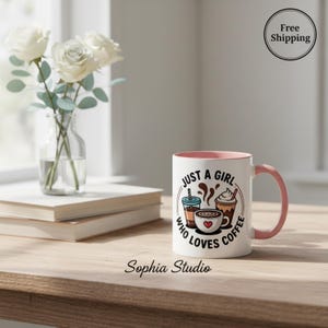 Op de afbeelding: Witte koffiemok met roze binnenkant en handvat. De mok heeft de tekst "JUST A GIRL WHO LOVES COFFEE" met koffie-illustraties. Een vaas met witte rozen staat ernaast.