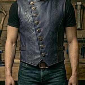May include: A navy blue leather vest with a high collar and gold buttons. The vest has a Celtic knot design and is worn with a black t-shirt and blue jeans. A brown belt is also visible.