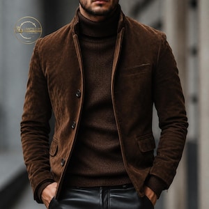 May include: A brown suede jacket with a high collar and button closure. The jacket is worn over a brown turtleneck sweater. The image shows a person wearing the jacket and sweater. The jacket has two pockets and a tailored fit.