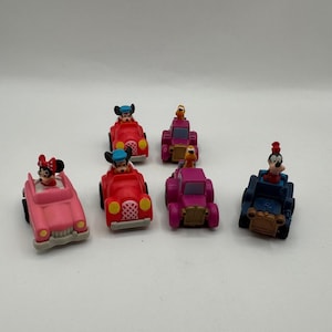Puede incluir: Una colección de seis coches de juguete con personajes de Disney. Los coches son de varios colores, incluyendo rosa, rojo y morado. Cada coche tiene un personaje diferente, como Mickey Mouse, Minnie Mouse y Goofy.