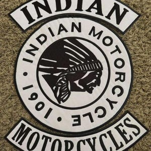 May include: A white and black embroidered patch featuring the words "INDIAN MOTORCYCLES" and a Native American profile. The patch also includes the year "1901". The patch is circular with curved text above and below.