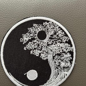 May include: Embroidered patch featuring a Yin and Yang design with a tree motif. The patch is circular, with a black and white color scheme. The tree is white, and the background is black. The patch is likely for clothing or accessories.