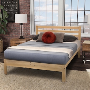 May include: A light-colored wooden bed frame with a headboard and footboard. The bed is made up with a blue comforter and a white blanket. Decorative pillows in shades of gray and red are arranged on the bed.