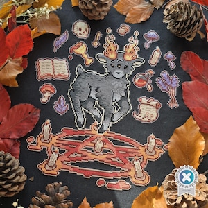 May include: A cross-stitch design featuring a gray goat with flaming horns standing on a candle-lit altar. The design includes a skull, potion bottles, mushrooms, and a book, set against a black background with autumn leaves and pine cones.