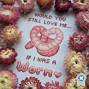 Könnte beinhalten: Kreuzstich-Kunst mit dem Text "WOULD YOU STILL LOVE ME... IF I WAS A WORM" und einem rosa Wurm-Design. Das Kunstwerk ist von getrockneten rosa und gelben Blumen umgeben.