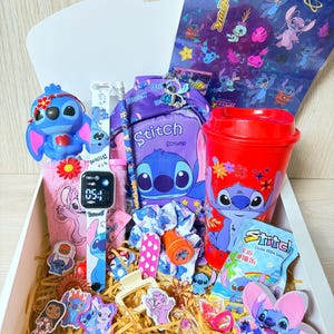 Può includere: Una scatola regalo piena di articoli a tema Stitch, tra cui una figura blu, un orologio digitale con cinturino a motivi, uno zaino viola, un bicchiere rosso, una matita, un elastico per capelli, una molletta, vari adesivi e ciondoli decorativi.
