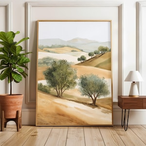 May include: A framed watercolour painting of a tranquil landscape with rolling hills and olive trees. The artwork uses warm earth tones, with shades of brown, tan, and green. The painting is displayed in a room with a wooden floor.