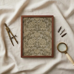May include: A framed floral print with a brown wooden frame. The print features a repeating pattern of large, stylized flowers in shades of beige and green. A brass compass, magnifying glass, and pen nibs are arranged around the frame.
