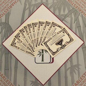 Peut inclure: Un &eacute;ventail de certificats de d&eacute;c&egrave;s Mahjong de style vintage, avec des bordures et du texte orn&eacute;s. Les certificats sont dispos&eacute;s sur un carr&eacute; blanc et rouge, avec un motif de bambou au centre. Le fond pr&eacute;sente un motif de bambou.