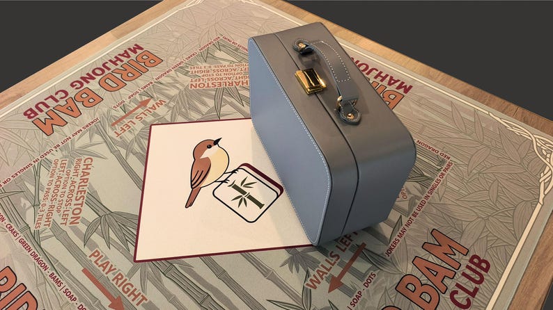 Puede incluir: Un malet&iacute;n de Mahjong azul claro con asa y cierre dorado descansa sobre un tablero de juego. Una tarjeta con una ilustraci&oacute;n de un p&aacute;jaro y el texto "BIRD BAM MAHJONG CLUB" est&aacute; frente al malet&iacute;n.