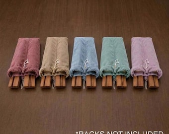 May include: Five folded fabric covers in dusty rose, tan, light blue, sage green, and lavender, each featuring a drawstring closure and visible wooden slats at the base. The text *RACKS NOT INCLUDED is printed in white at the bottom.