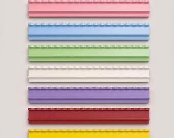 May include: A set of seven rectangular wall shelves arranged vertically, each featuring a top edge with a repeating semi-circular scalloped design. The shelves are colored in pink, light blue, light green, white, purple, red, and yellow.