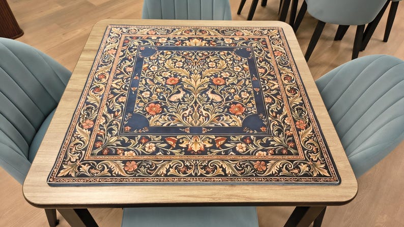 K&ouml;nnte beinhalten: Quadratischer Holztisch mit detailliertem Blumenmuster in Marineblau, Beige und Orange. Der Tisch ist von hellblauen St&uuml;hlen umgeben. Das Design des Tisches weist komplizierte Muster auf.
