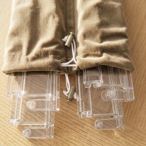May include: A tan velvet drawstring pouch containing several clear, articulated plastic components. The pouch features a white cord with two metallic cylindrical toggles at the ends, securing the contents inside the soft, textured fabric bag.
