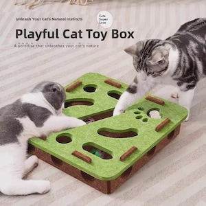 May include: A playful cat toy box with a green felt top and brown sides. The box has various cutouts and wooden accents. Two cats are interacting with the toy. Text on the image reads "Playful Cat Toy Box" and "Unleash Your Cat's Natural Instincts."