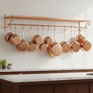 May include: A kitchen with a copper pot rack holding several copper pans. The kitchen features dark wood cabinets, a marble countertop, and a large window. The pots are suspended above a countertop.