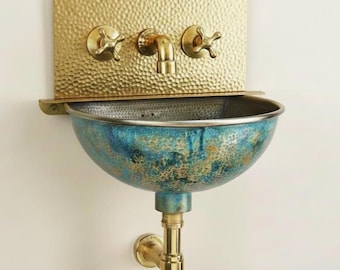 Lavabo mural de latón martillado con cubeta de cobre verdigrís y grifo de peltre con manija en cruz.