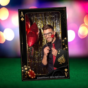 Peut inclure: Un accessoire de photomaton en forme de carte à jouer avec un homme posant à l'intérieur. La carte est noire avec des accents dorés et l'As de Pique. Le photomaton porte l'inscription "Jonathan's 30th Birthday". Des ballons et accessoires rouges sont visibles.