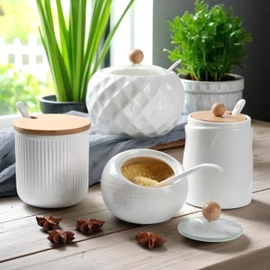 Puede incluir: Un conjunto de botes y cuencos de cocina de cerámica blanca con tapas y cucharas de madera. Los botes presentan diferentes texturas, incluyendo patrones acanalados y de diamantes. Especias de anís estrellado sobre la superficie de madera.