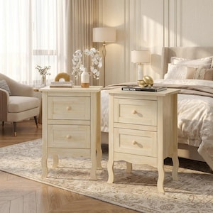 May include: Two light-colored wooden nightstands, each featuring two drawers with round knobs and curved legs. The nightstands are positioned on either side of a bed, with one holding a white vase with flowers and the other a book titled Marc Hom.