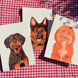 May include: Three rectangular art prints featuring detailed coloured pencil illustrations of dogs. The left print shows a black and tan dog, the centre print depicts a German Shepherd, and the right print displays a fluffy orange-brown dog.