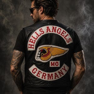 Puede incluir: Un chaleco de cuero negro con un gran parche bordado en la espalda que muestra el texto HELLS ANGELS en un arco blanco, un emblema central de calavera alada, las letras MC y la palabra GERMANY en un arco blanco en la parte inferior.