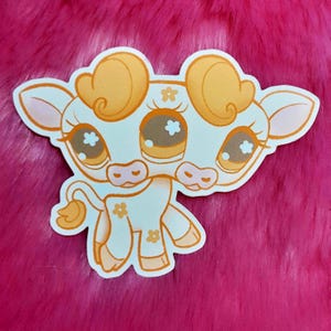 May include: A die-cut sticker featuring a cartoon cow with a cream-colored body and orange accents. The cow has large brown eyes, flower details, and a curled tail. The sticker is on a pink, fuzzy background.