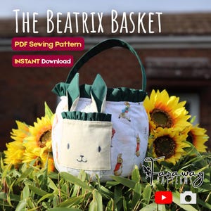 May include: A white fabric basket with a green handle and bunny ears, featuring a pocket with a bunny face. The basket is decorated with a Peter Rabbit pattern and the text "The Beatrix Basket". Sunflowers and greenery surround the basket.