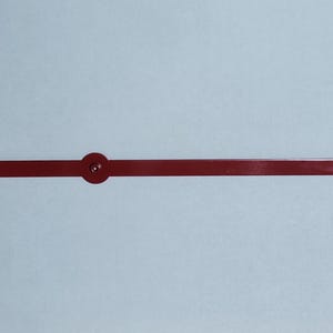 May include: A red clock hand with a circular end and a small circular detail in the middle. The hand is a straight, rectangular shape. The background is a light blue color.